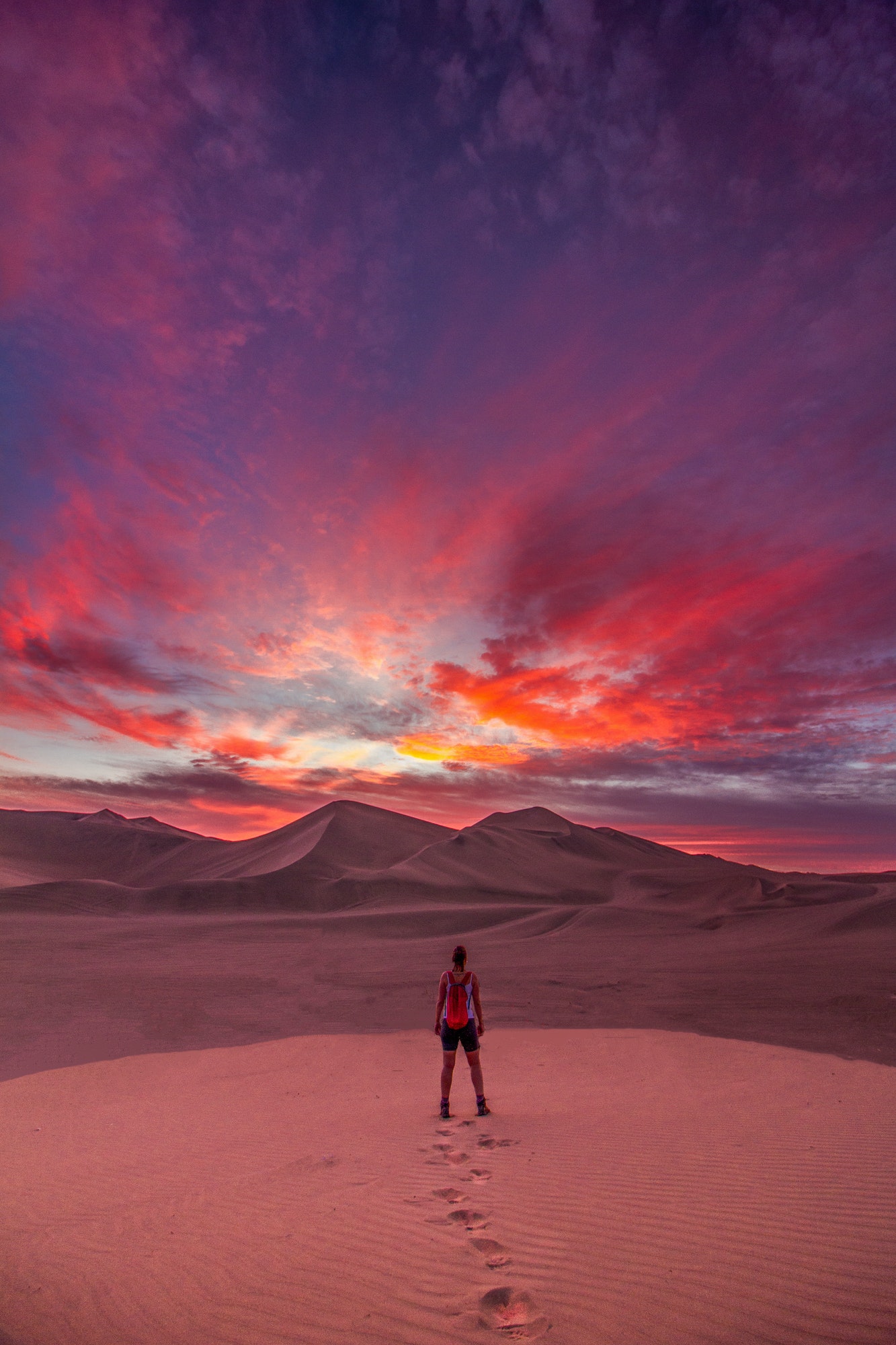 An adventurous girl contemplating the incredible colorful sky in the desert of Huacachina - Ica -