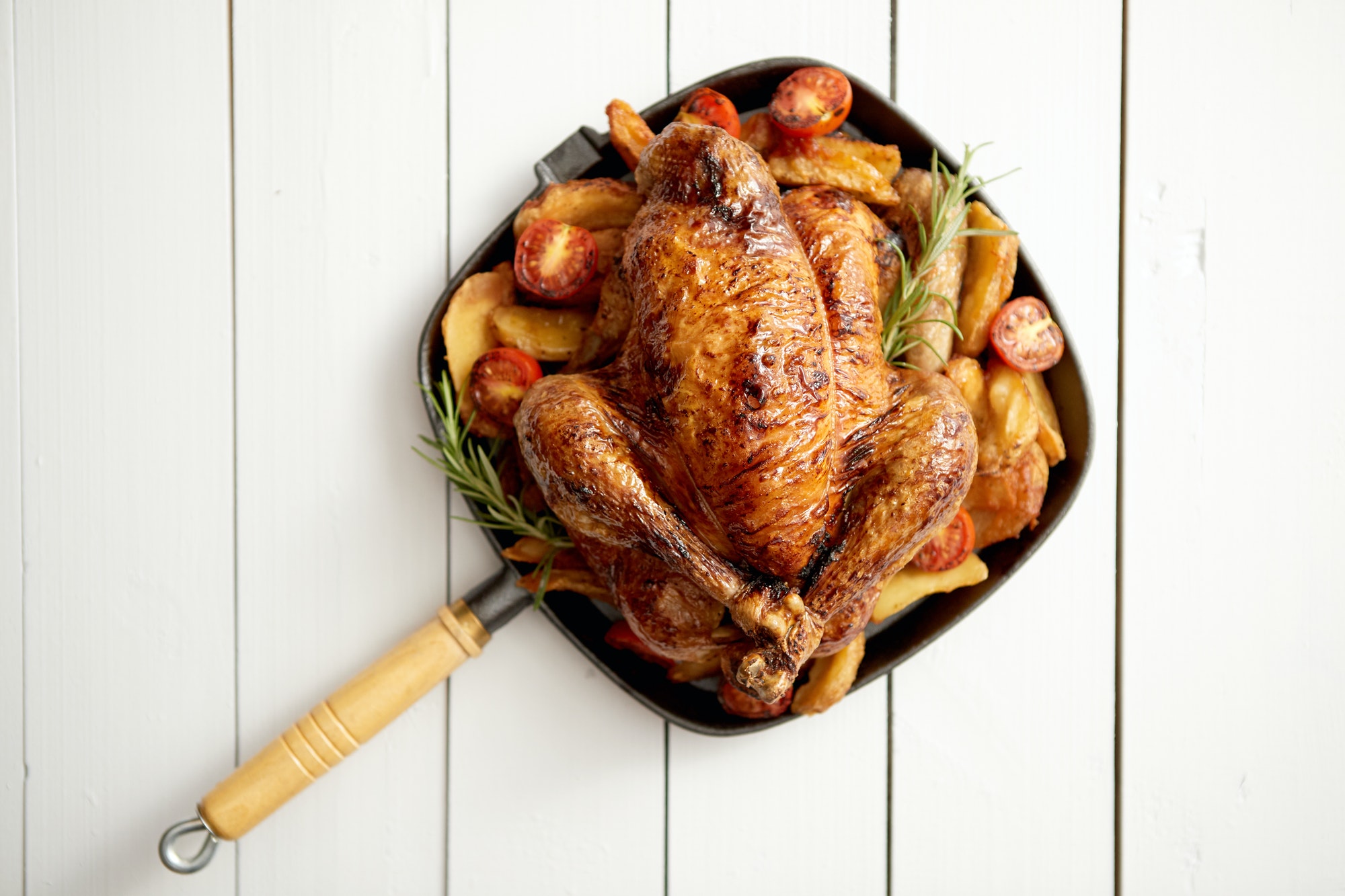 Grilled whole chicken in cast iron black pan with potatoes, tomatos and rosemary